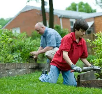 man in red polo shirt and blue denim jeans sitting on brown wooden bench during daytime