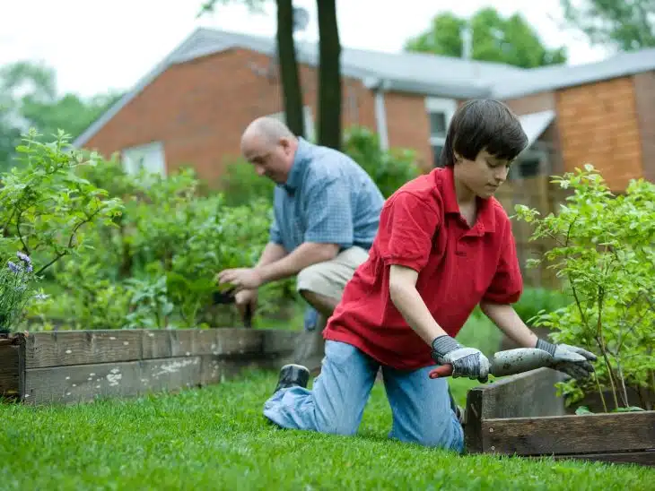 man in red polo shirt and blue denim jeans sitting on brown wooden bench during daytime